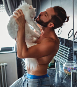 Shirtless man kissing his pet cat in the kitchen